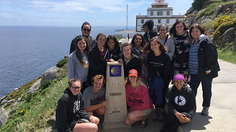 Students pose around a stone plinth marking the compostela del camino de santiago.